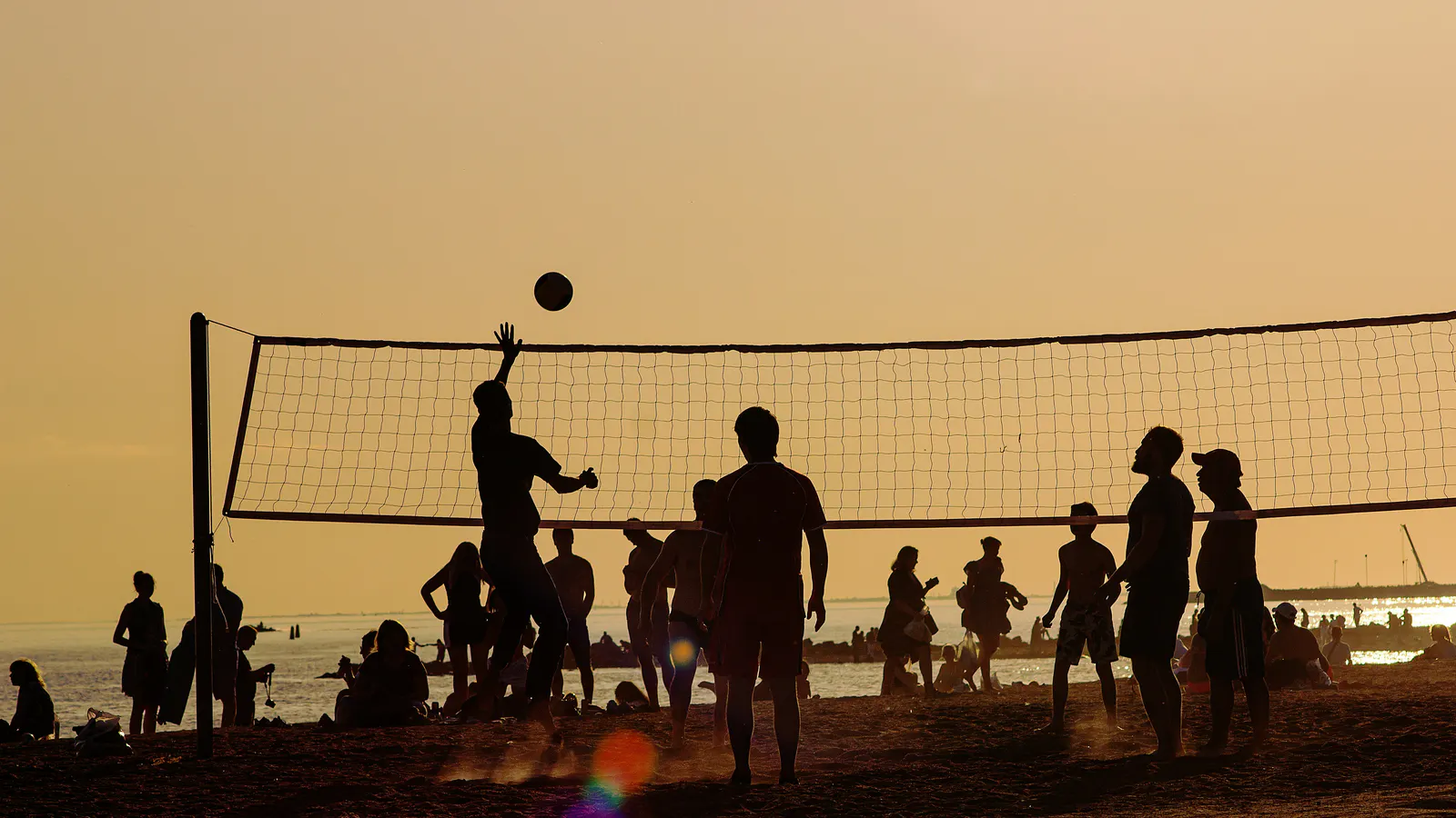 Groupe jouant au volley sur la plage au coucher du soleil pendant une activité d'équipe